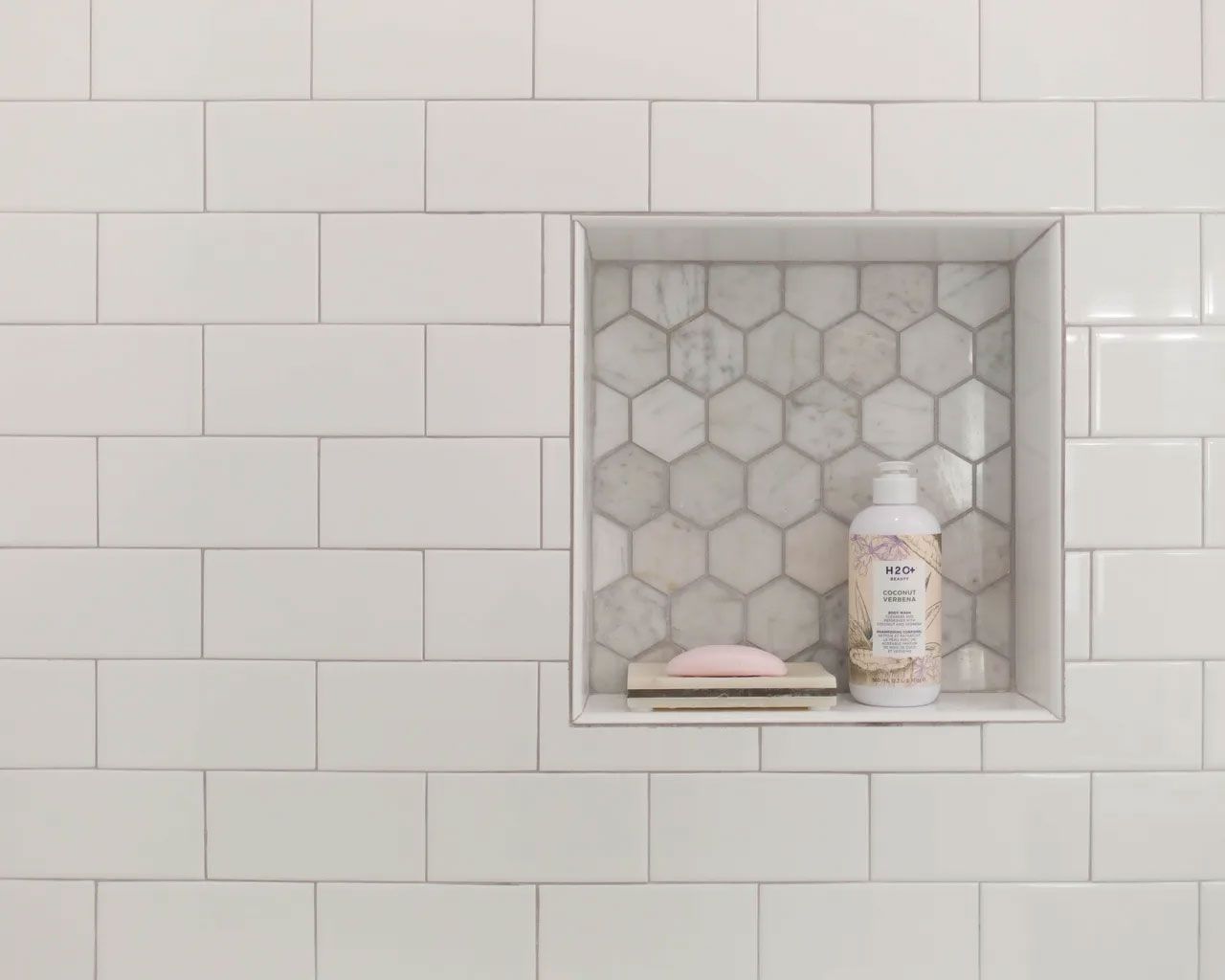 A shower niche with white tiles and a bottle of soap.