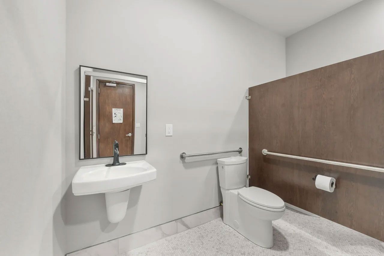 A bathroom with a toilet , sink and mirror.