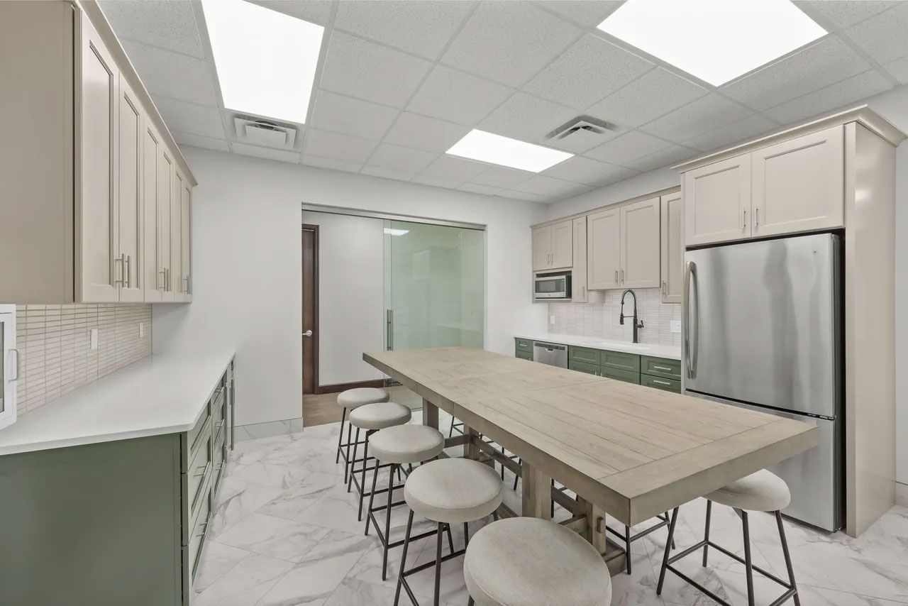 A kitchen with a long table and stools and a refrigerator.