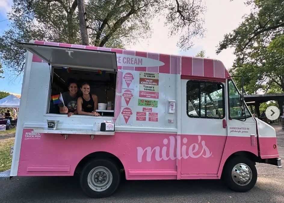 A pink and white ice cream truck is parked in a parking lot.