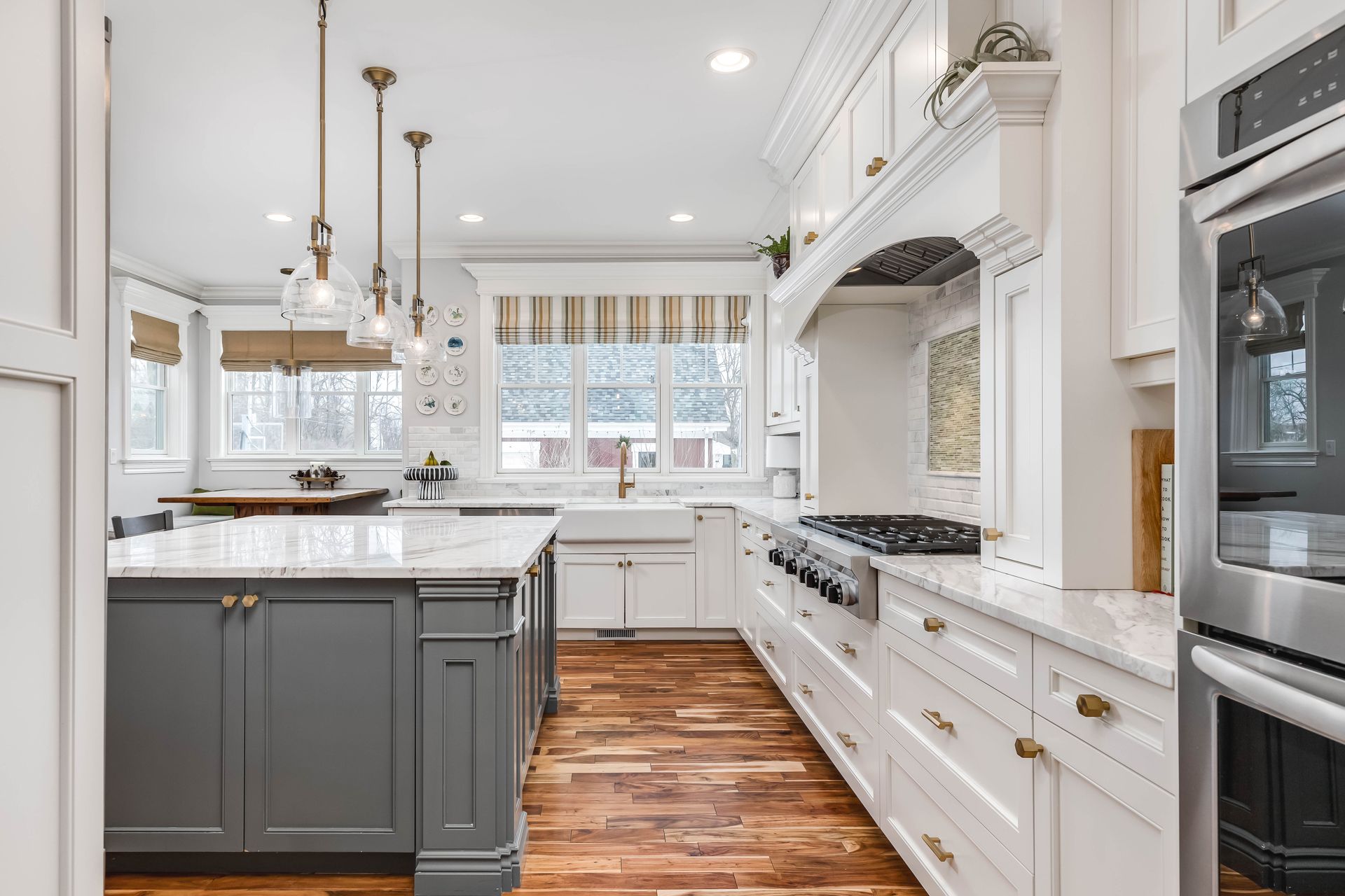 A modern kitchen with a gray island, white cabinets, marble countertops, pendant lights, and hardwood floors.