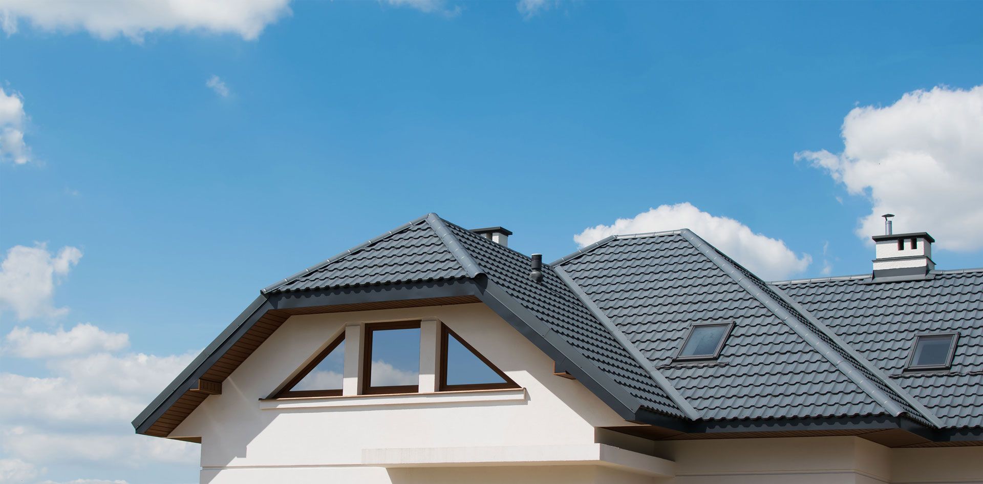 White house roof with gray shingles under a blue sky with clouds