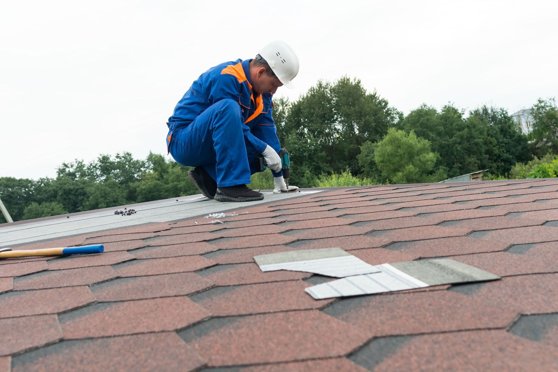Worker in blue safety gear repairing shingles on a rooftop.