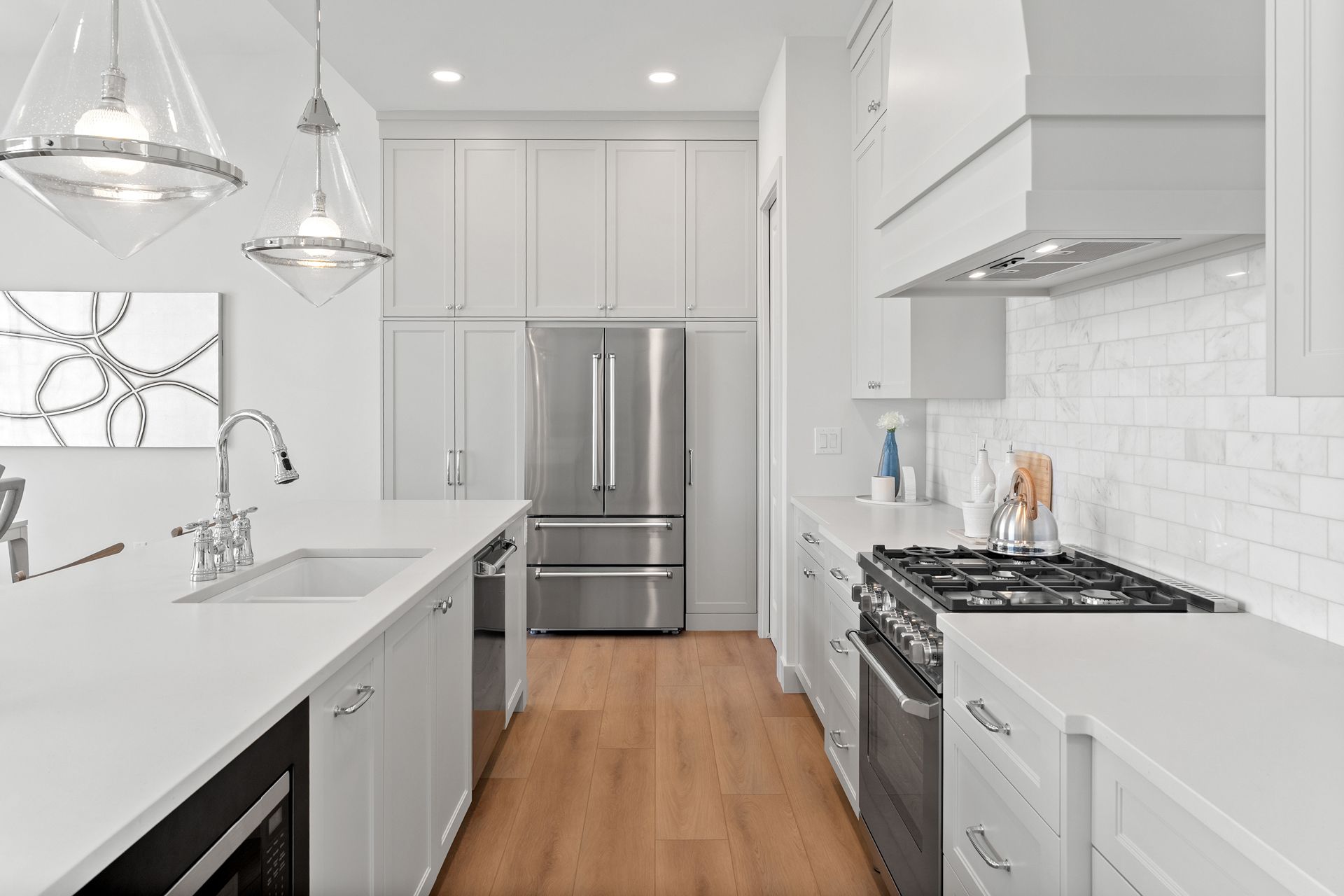 A modern, bright kitchen with white cabinetry, stainless steel appliances, a center island with sink, and wood flooring.