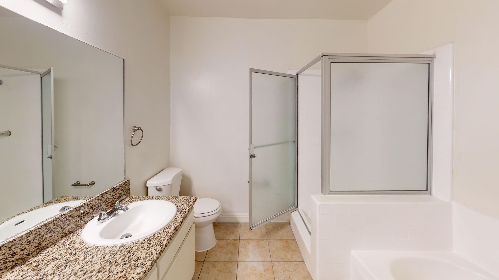Bathroom with a vanity, toilet, and a shower with a glass door. White walls, beige floor.