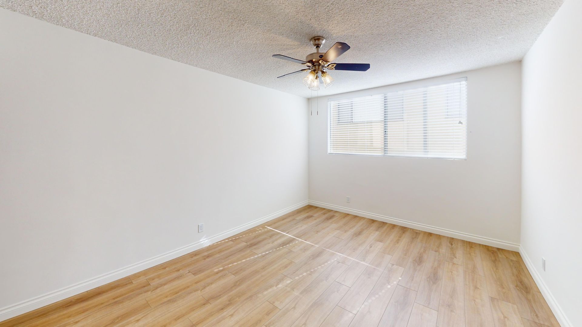 Empty room with wood-look flooring, white walls and ceiling, window, and ceiling fan.