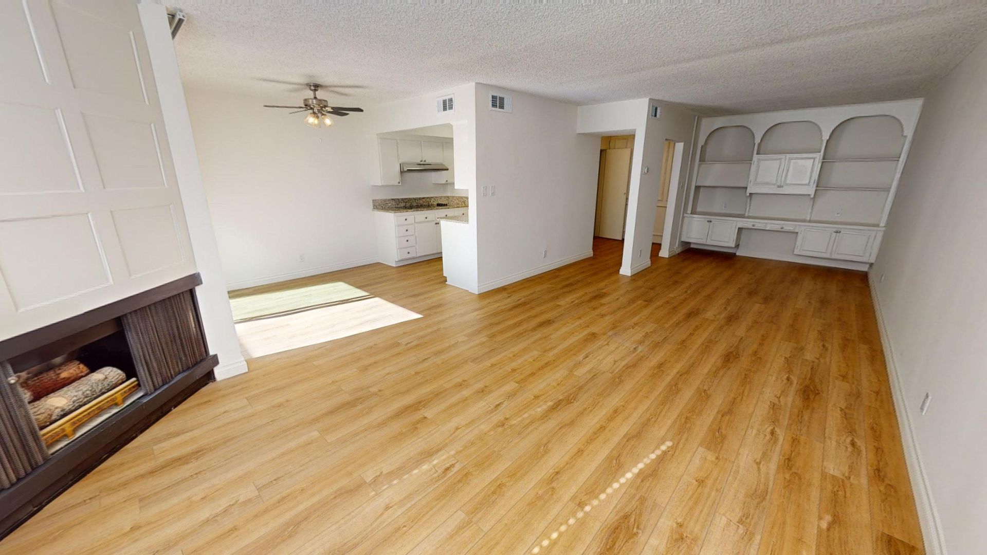 Living room interior with hardwood floors, built-in shelving, fireplace, and kitchen visible.