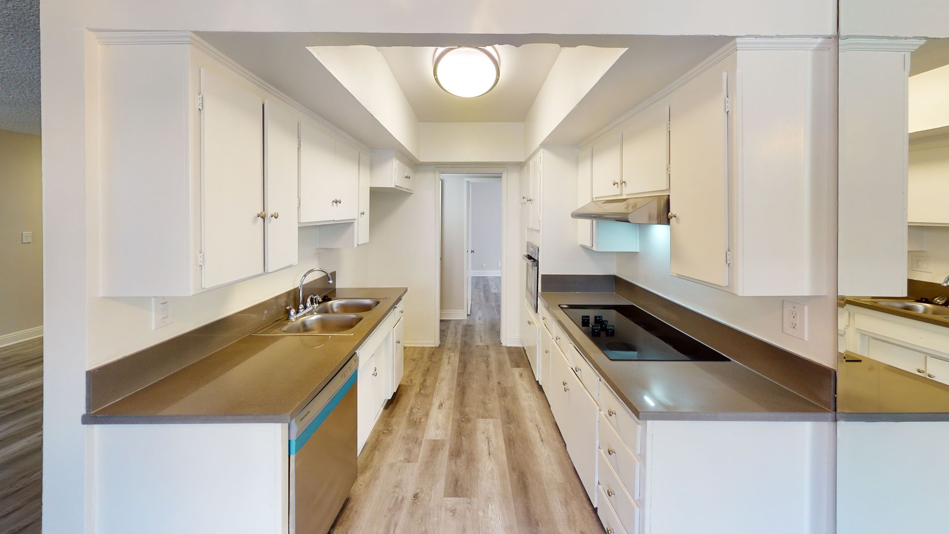Narrow kitchen with white cabinets, gray countertops, and light wood-look flooring.