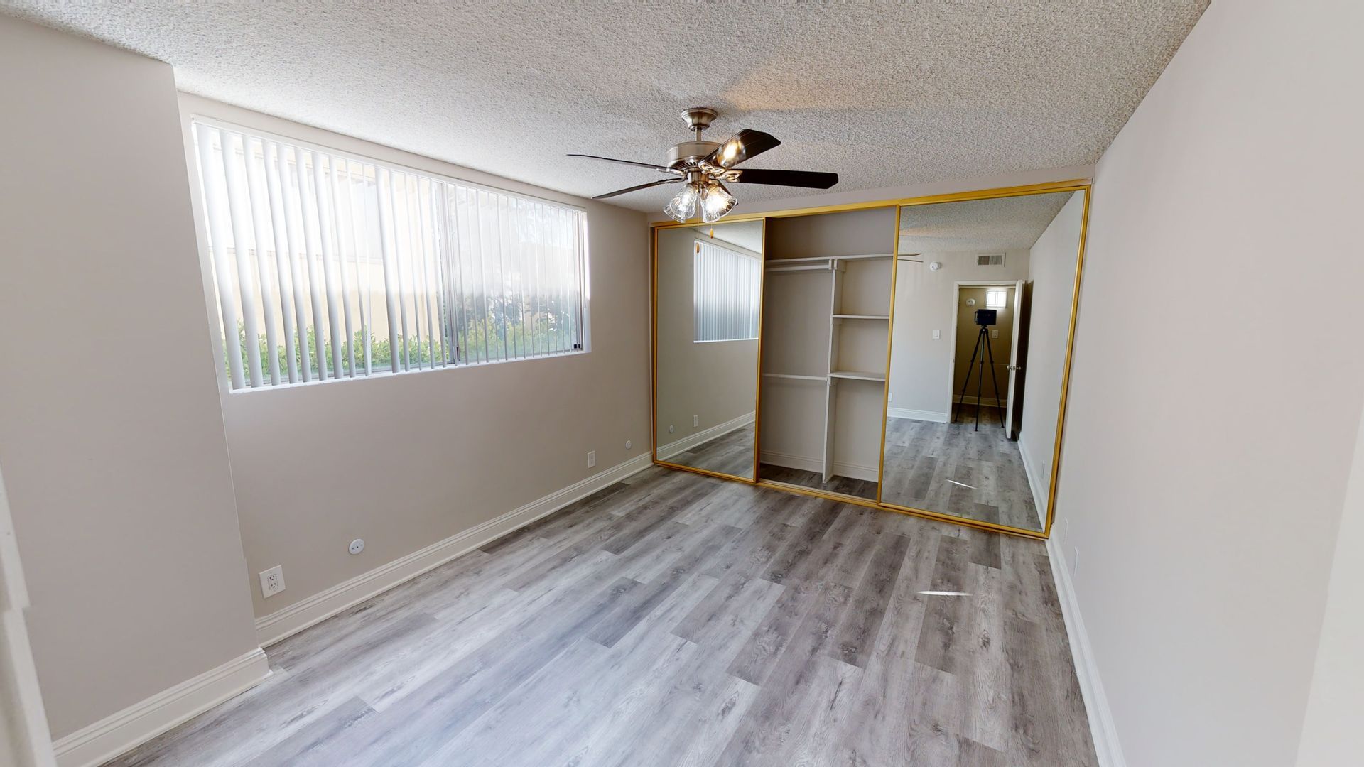 Bedroom with gray wood-look flooring, large mirrored closet, a window with blinds, and ceiling fan.