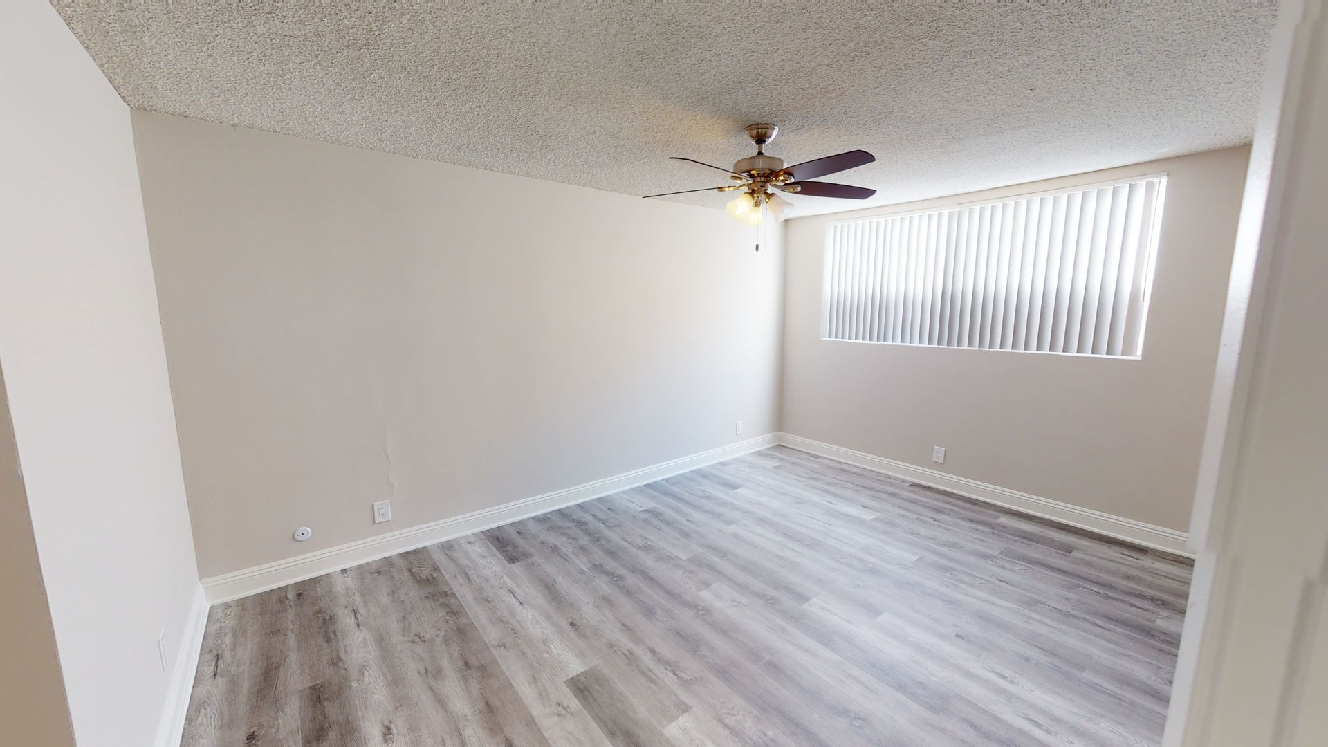 Empty room with wood-look floor, window with blinds, ceiling fan, and light-colored walls.