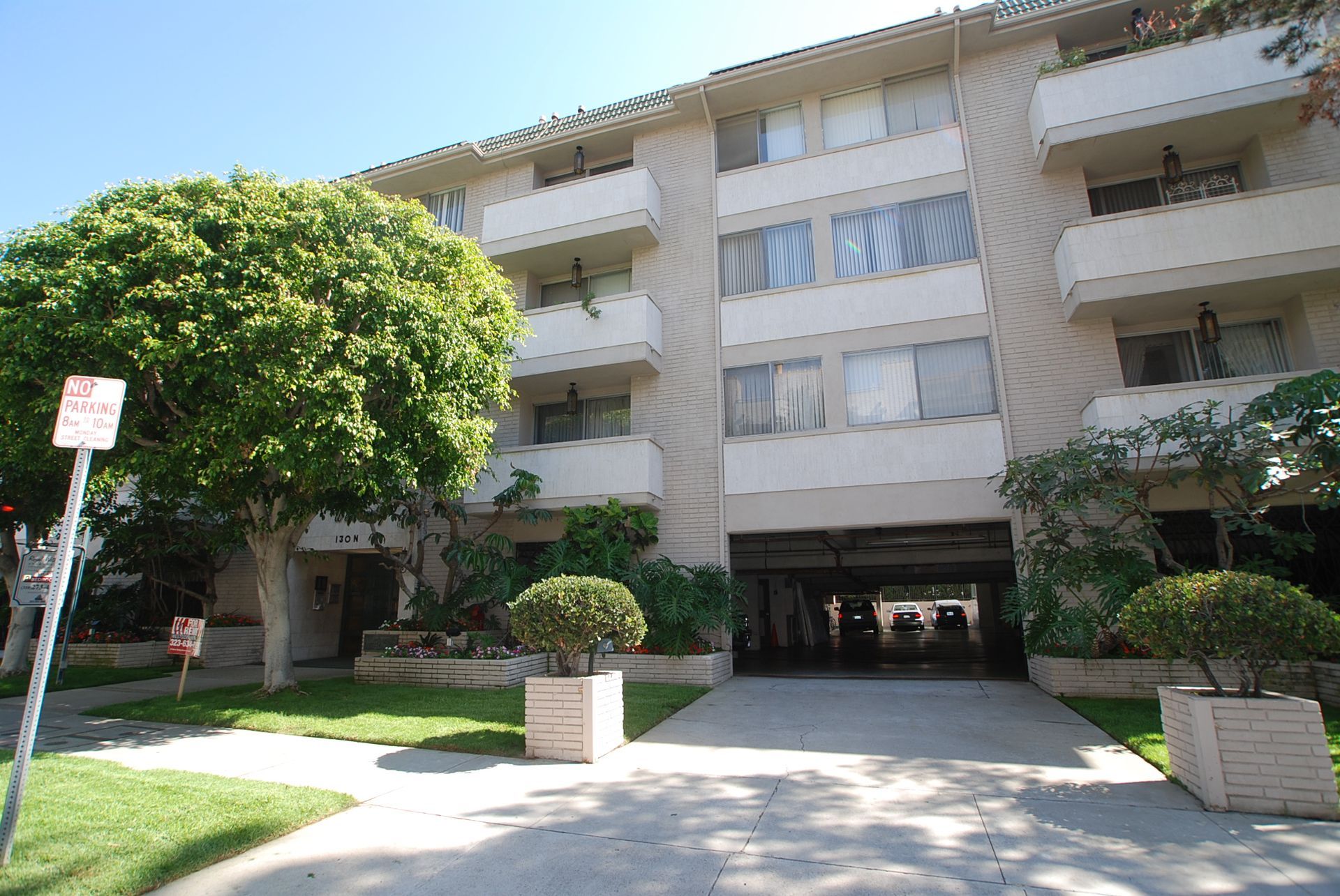 Apartment building with balconies and driveway entrance, flanked by trees and planters.