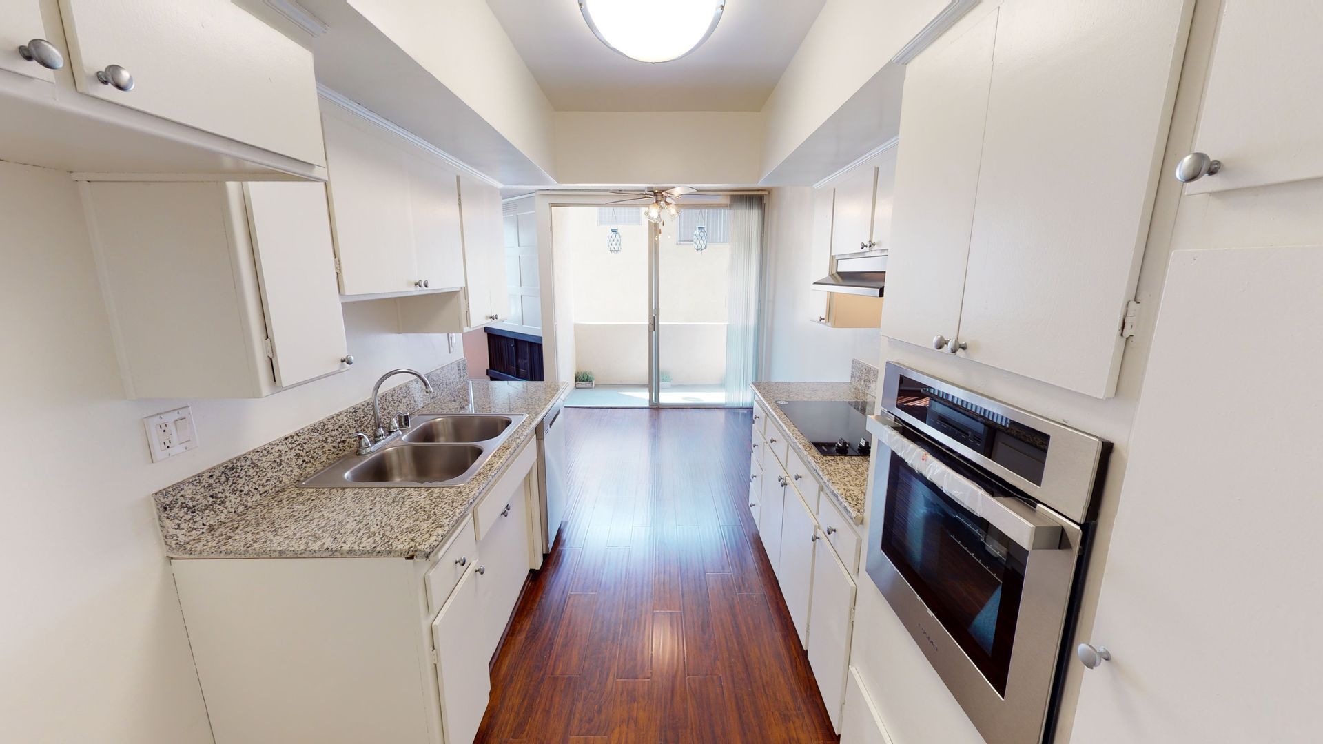 Bright kitchen with white cabinets, granite countertops, and a stainless steel oven.  View opens to a balcony.