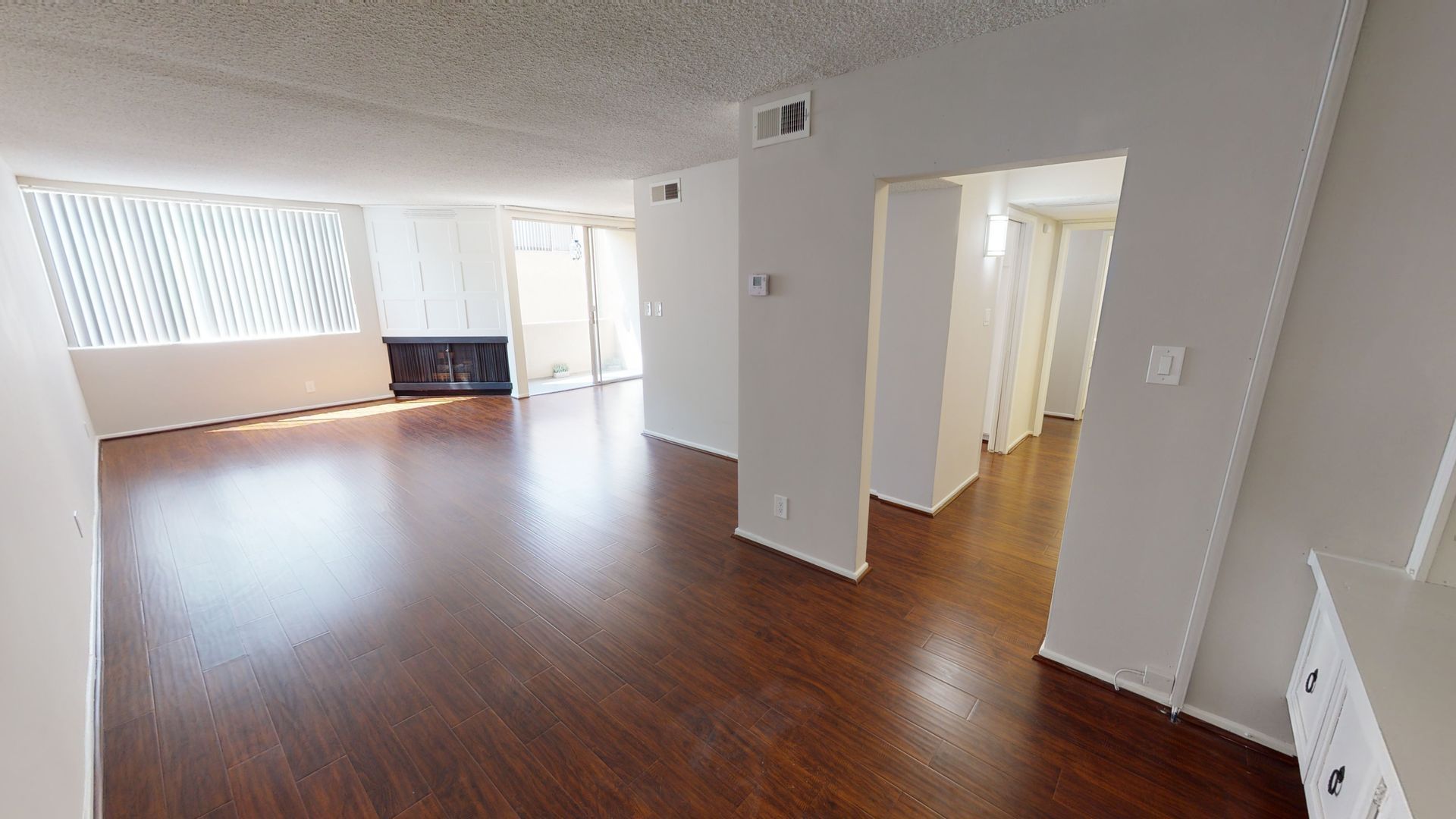 Empty living room with dark wood flooring, fireplace, and window with blinds.