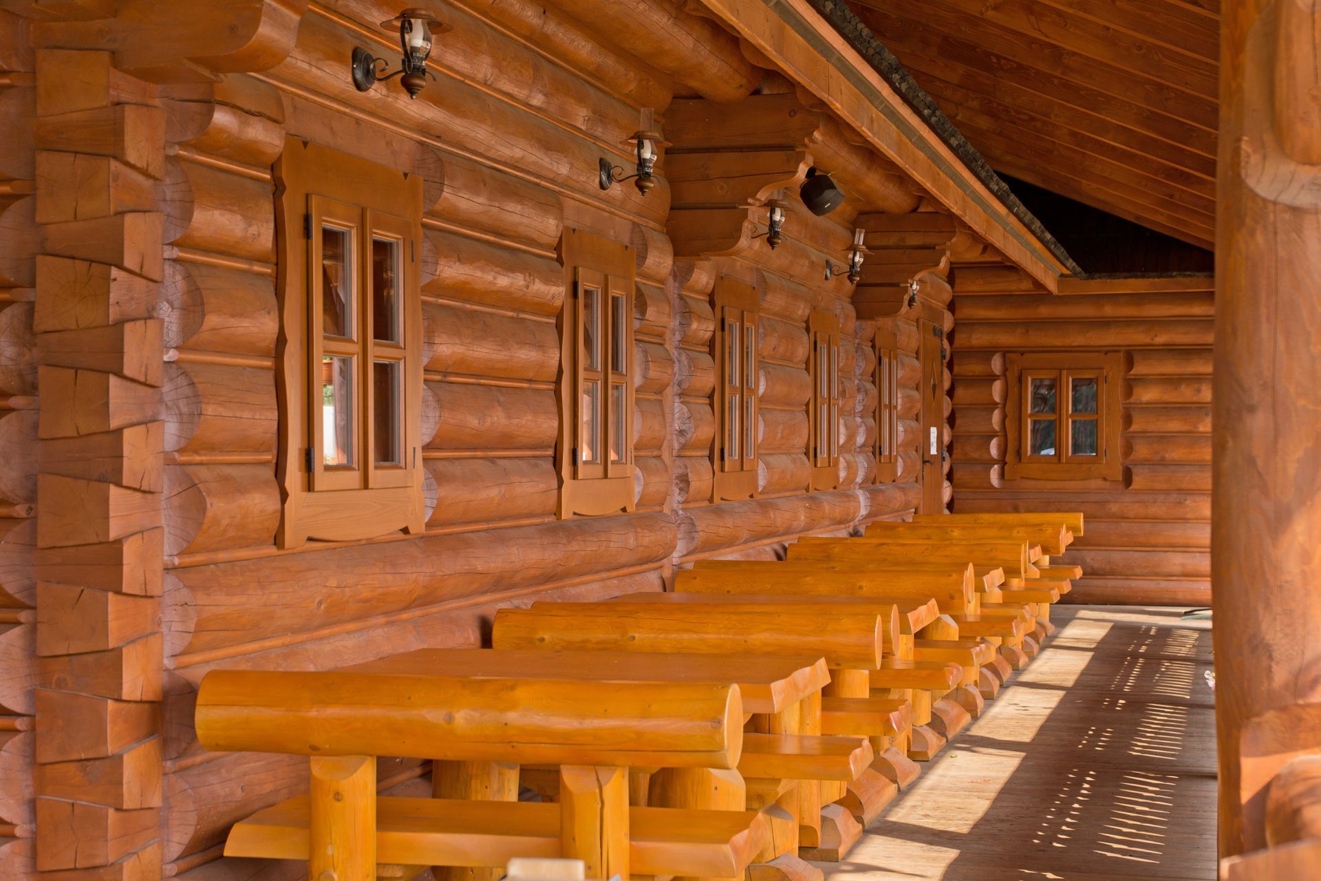 Wooden log cabin exterior with multiple tables and windows under a covered porch.