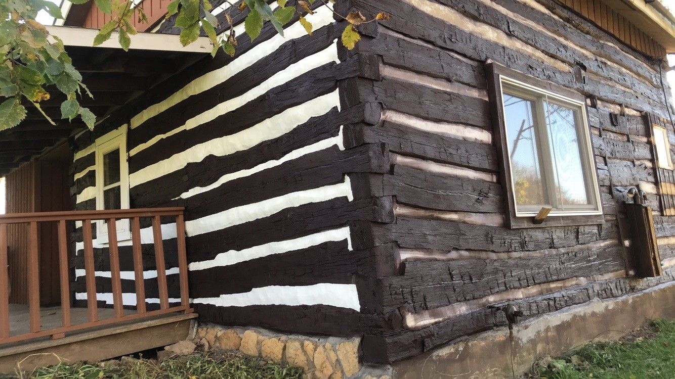 A black and white log cabin with a porch and a window.
