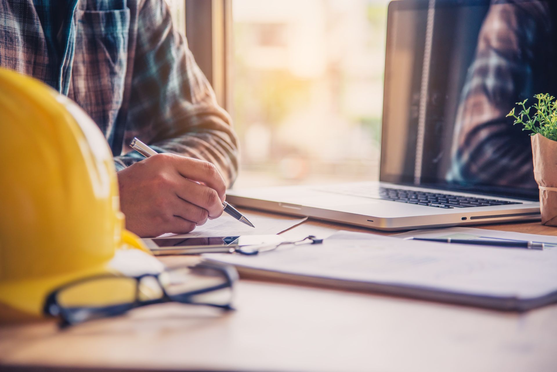 A man is sitting at a desk with a hard hat and a laptop.