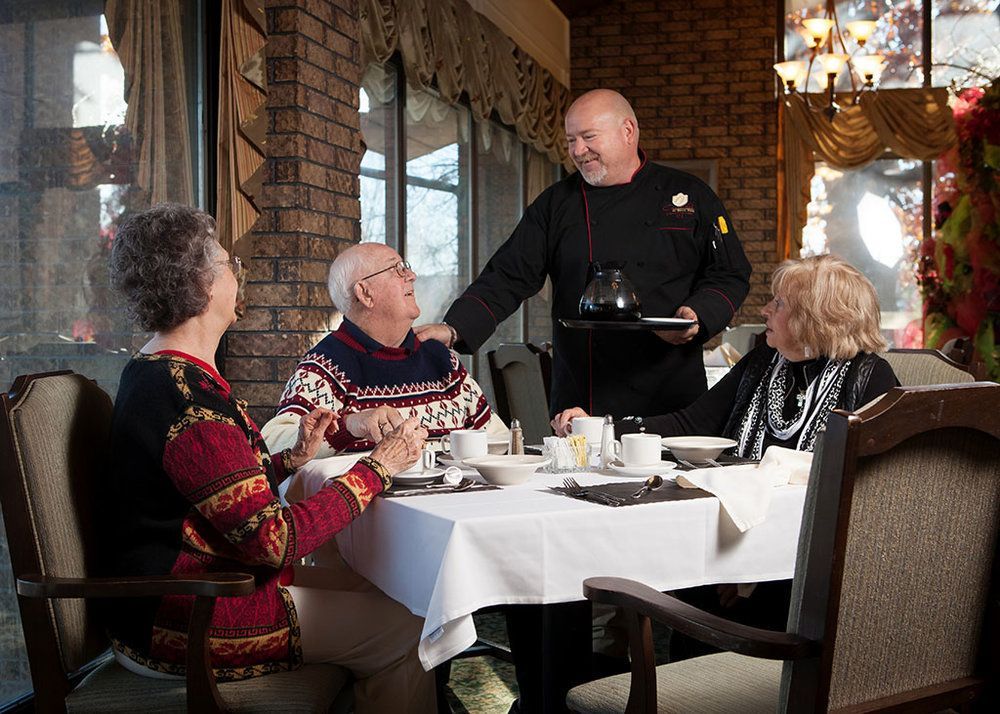 A man is serving food to a group of people sitting at a table.