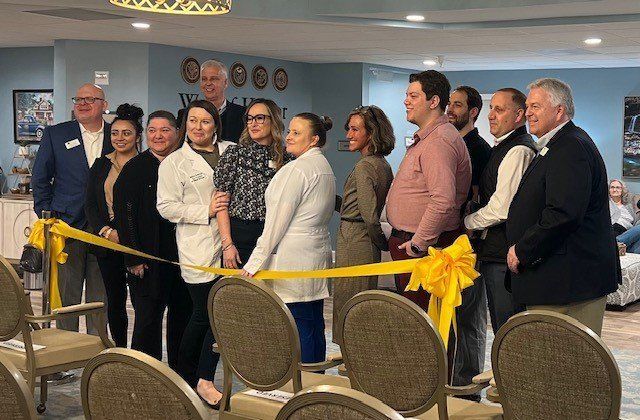 A group of people are cutting a yellow ribbon in a room.