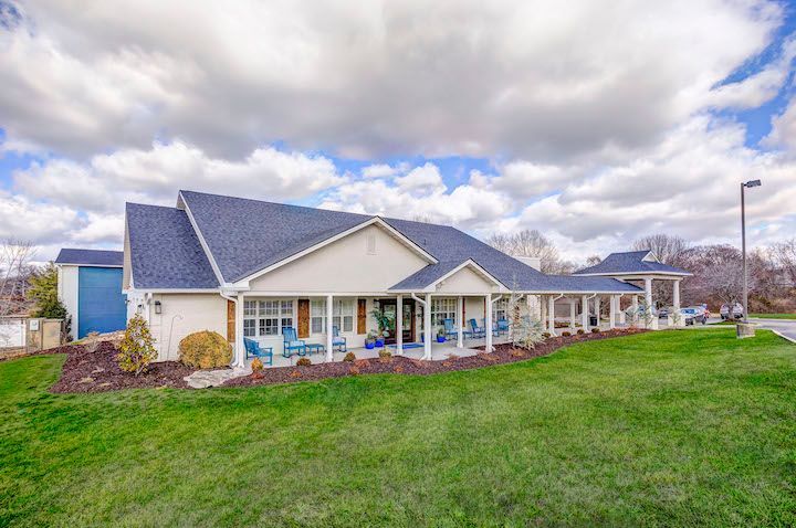 A large white house with a blue roof is sitting on top of a lush green lawn.
