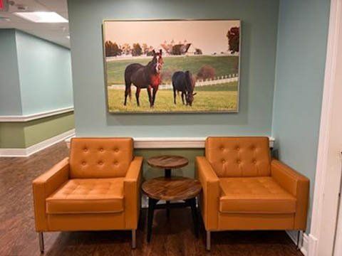 There is a painting of horses on the wall above the chairs.