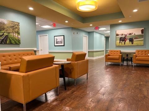 A living room with a couch , chairs , tables and a painting of horses on the wall.