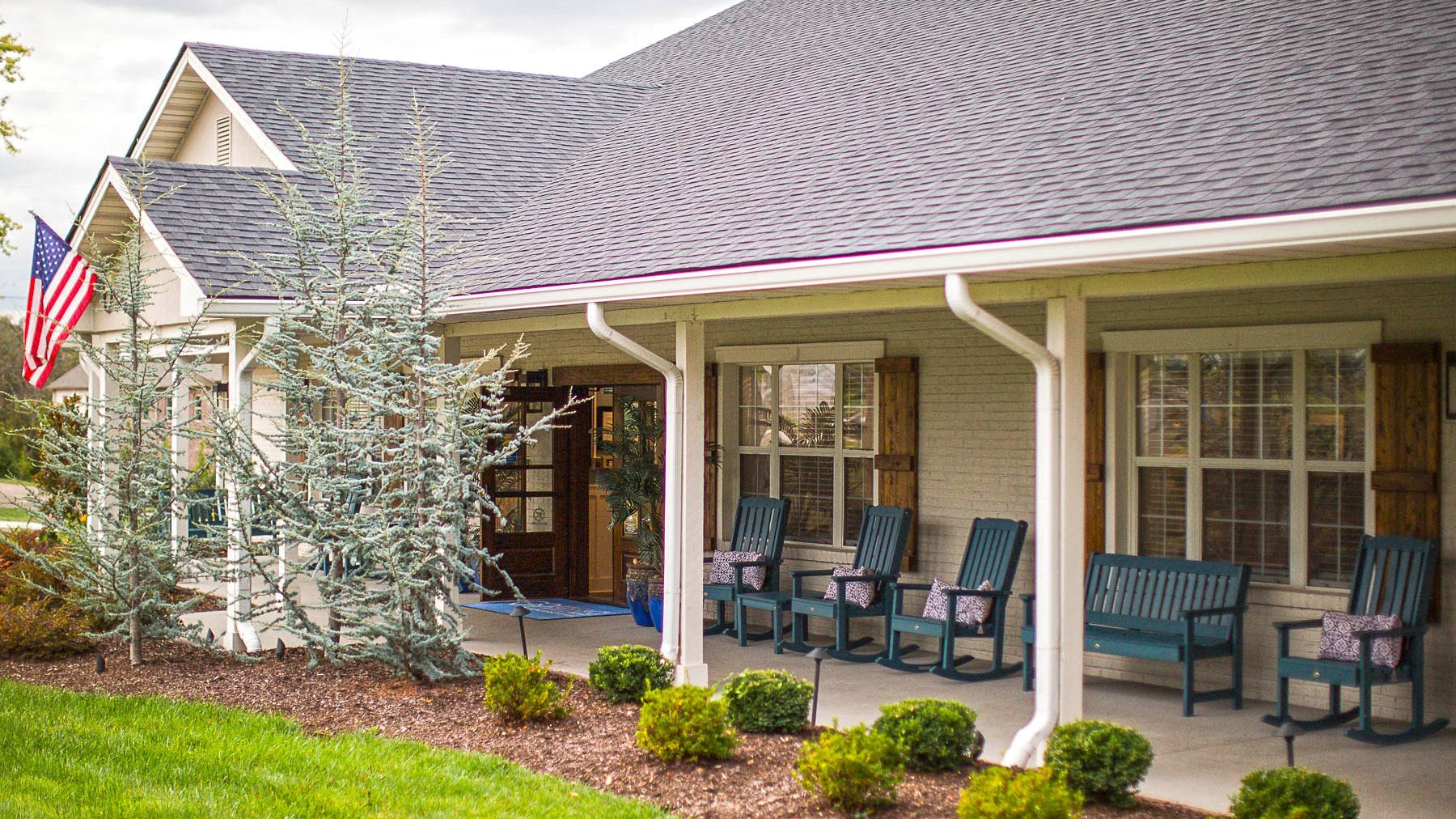 A porch with rocking chairs and a bench in front of a house.