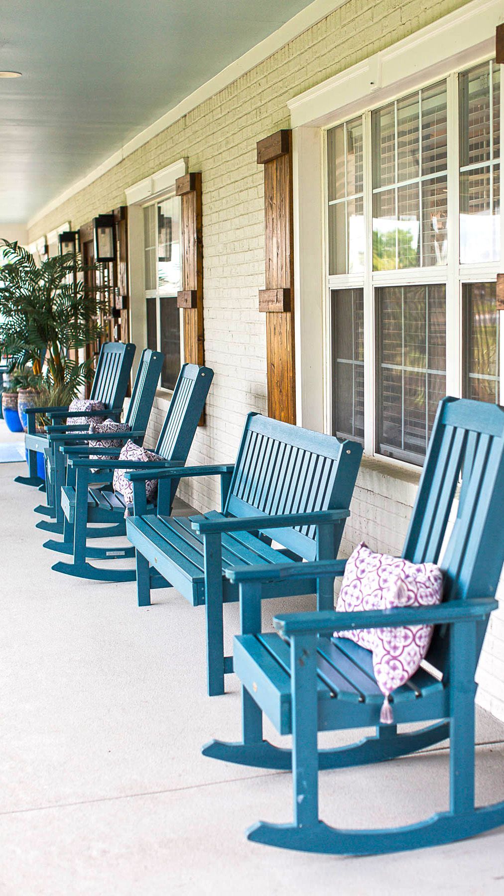 A row of blue rocking chairs on a porch next to a window.