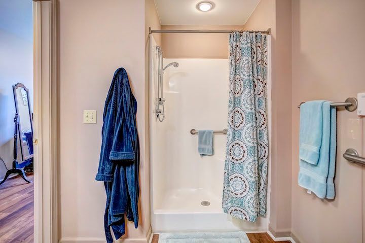 A bathroom with a walk in shower and a blue robe hanging on the wall.