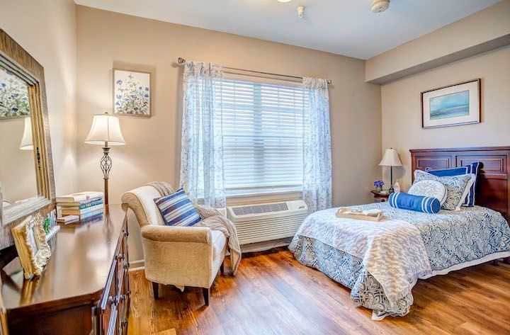 A bedroom with a bed , chair , dresser and mirror.