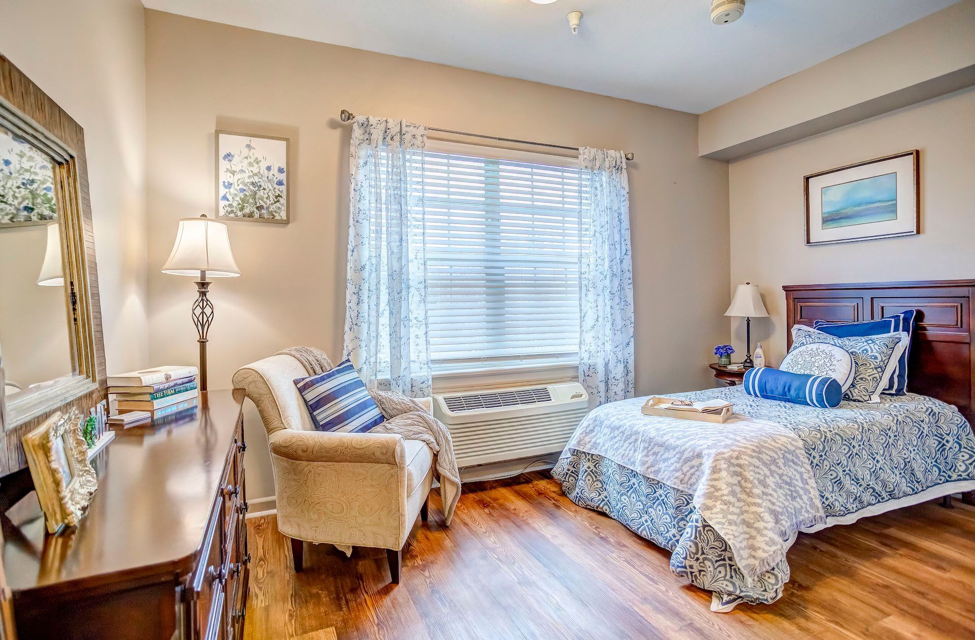 A bedroom with a bed , chair , dresser and mirror.