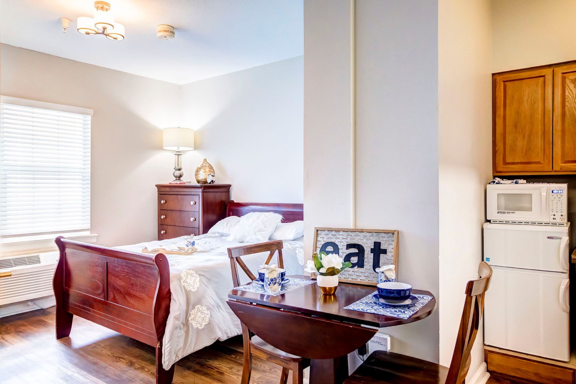 A bedroom with a bed , table , chairs and a sign that says eat.