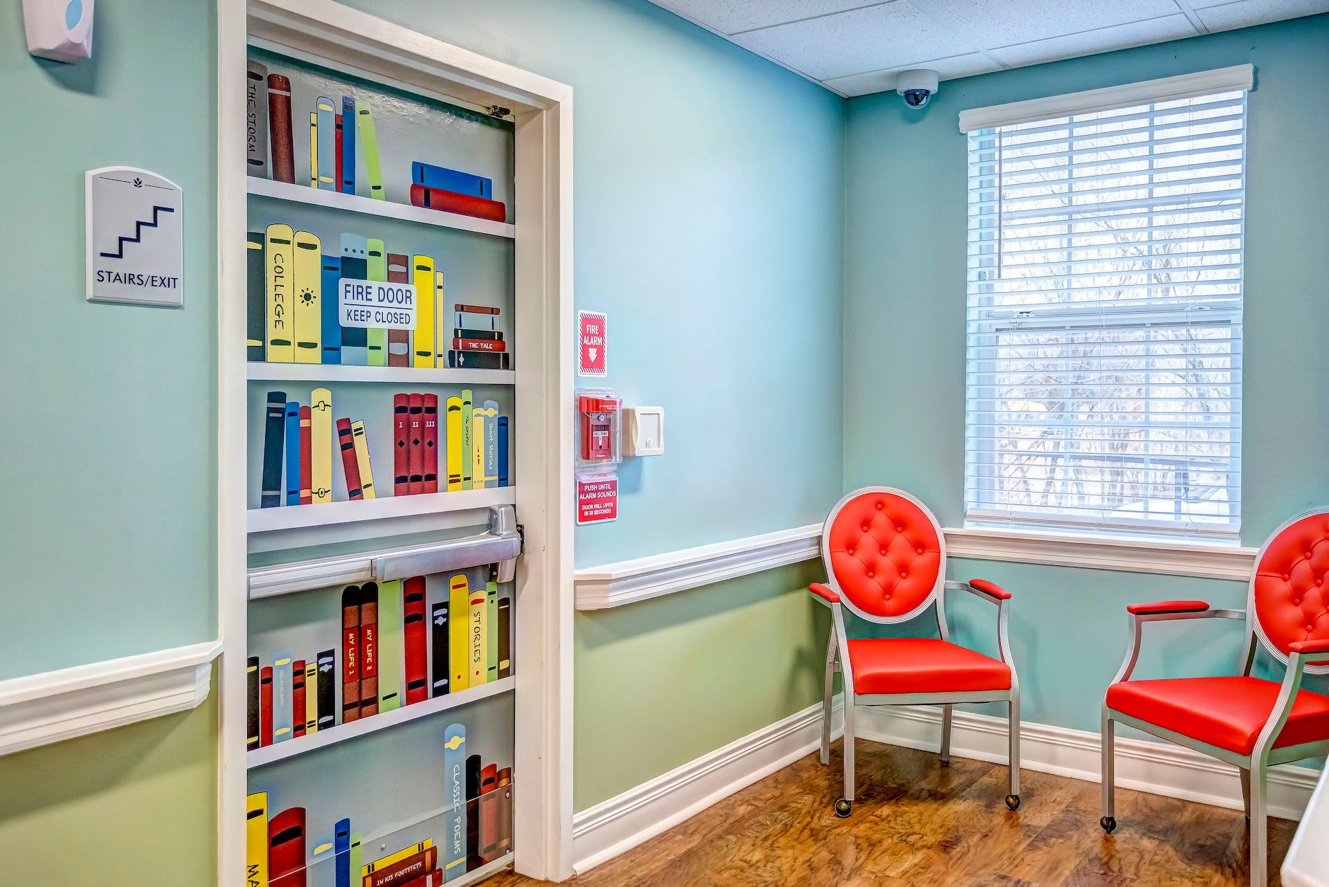 A waiting room with two red chairs and a bookshelf filled with books.