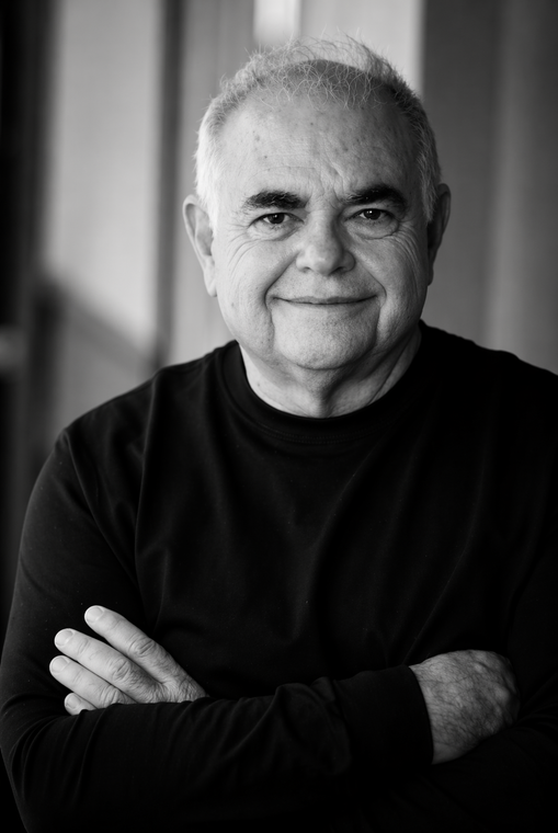 A man in a tuxedo with a red pocket square is smiling.