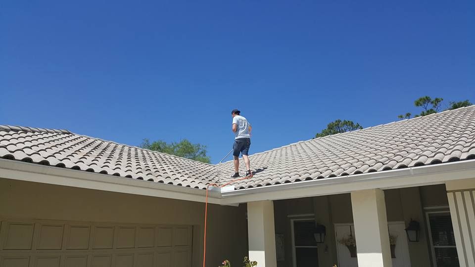 A person standing on a tile roof, cleaning a gutter on a sunny day.