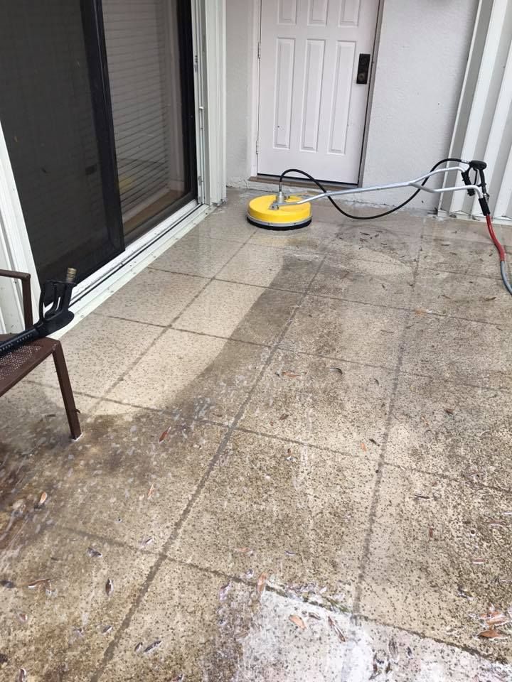 A person power washes a patio with a yellow surface cleaner. 