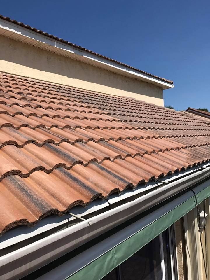 Brown tiled roof on a beige building with a blue sky in the background. A green gutter runs along the edge.