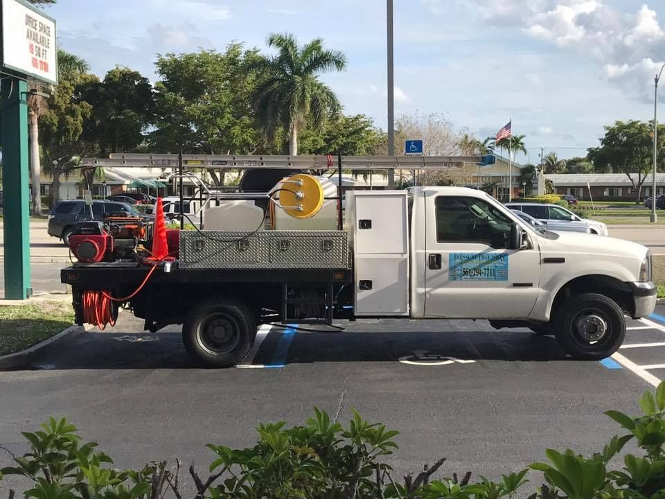 White work truck parked in a parking space with a side view of its equipment. Includes a sign and trees in the background.