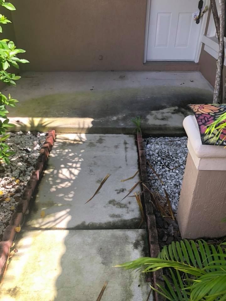 Concrete pathway leading to a white door, bordered by brick and gravel.
