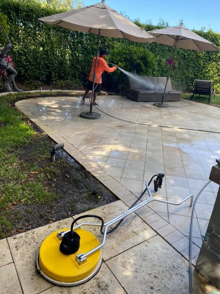 Person pressure washing a stone patio with a yellow surface cleaner. 