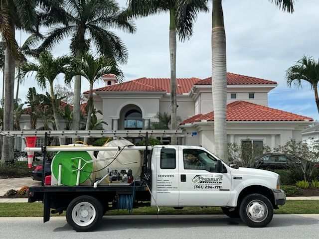 White truck with tanks parked in front of a large house with a red tile roof; palm trees in the background.