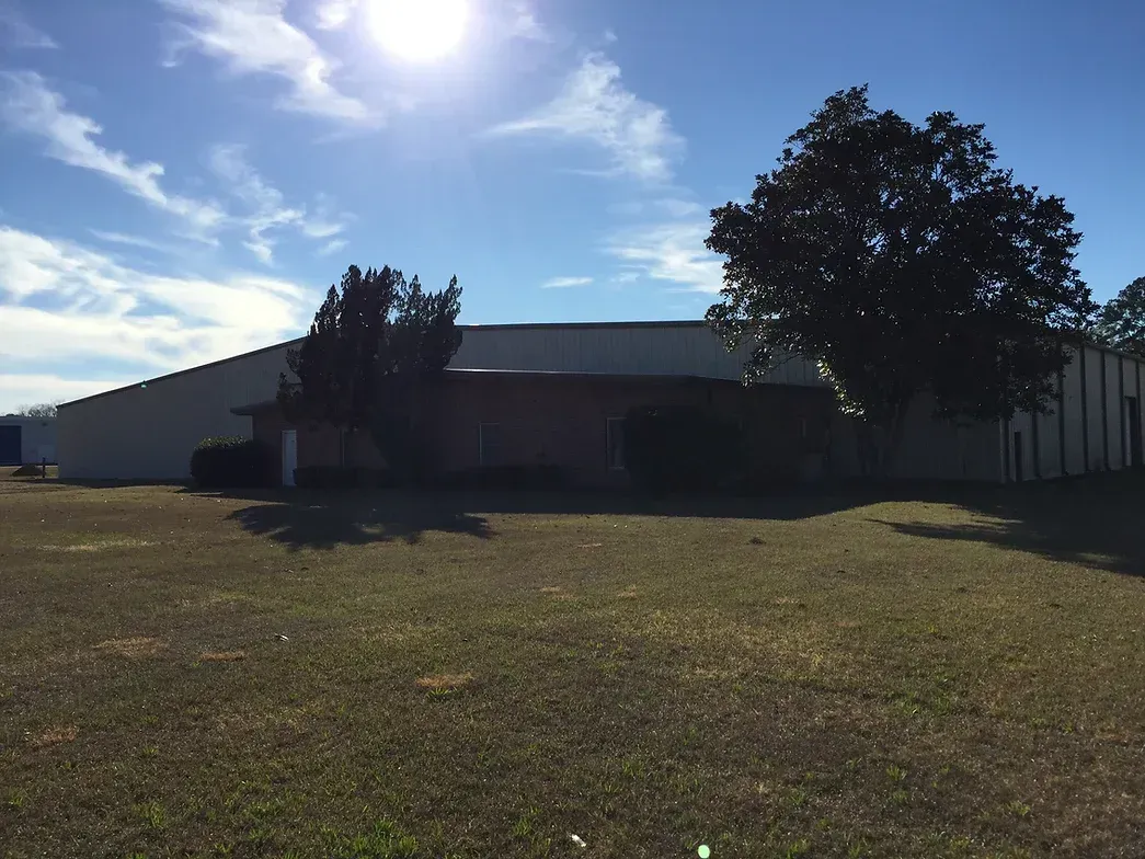 A large white building is sitting in the middle of a grassy field.