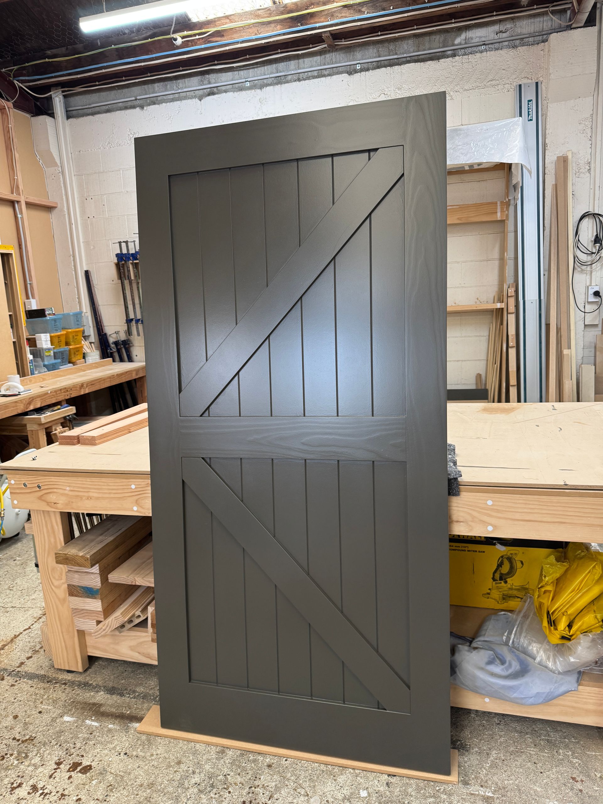 A dark gray barn door with a Z-brace design, standing upright in a wood workshop.
