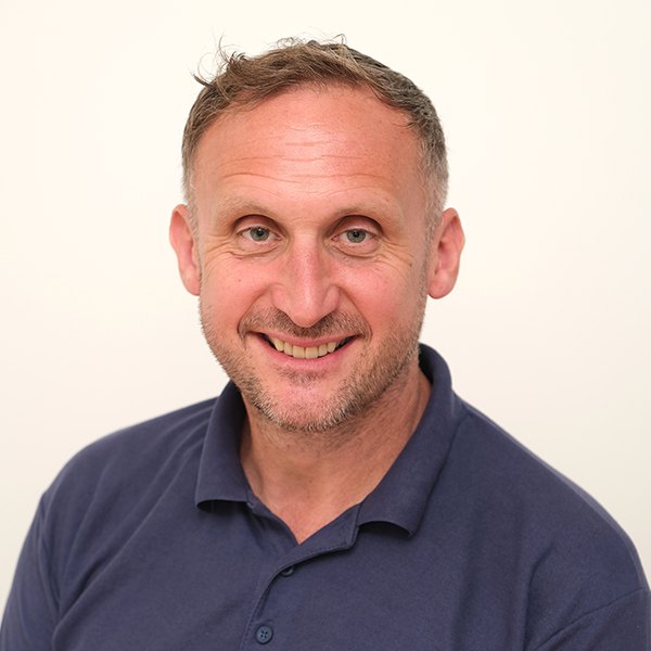 A man with a beard is smiling for the camera while wearing a blue polo shirt.