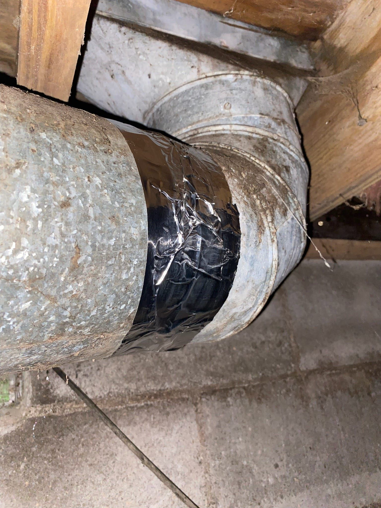 Metal ductwork elbow with black tape in a basement.