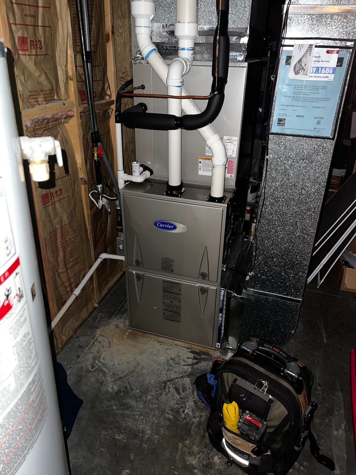 Furnace and water heater in a basement. Technician's tool bag on the floor.