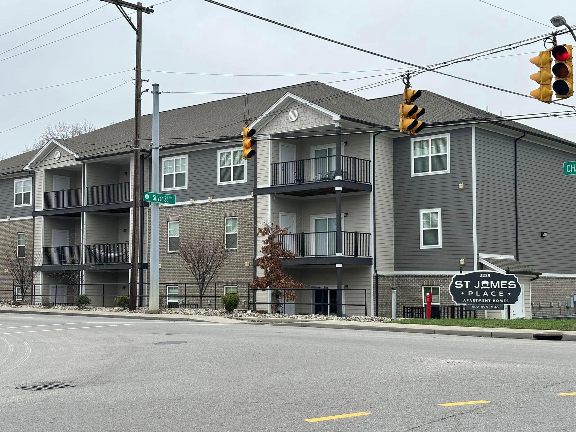 Apartment building at an intersection. Gray and white facade with balconies and a sign that says 