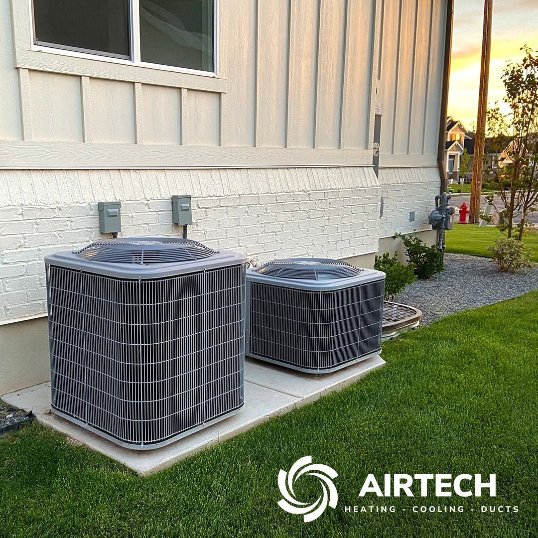 Two air conditioning units beside a house on a concrete pad, on a grassy lawn.