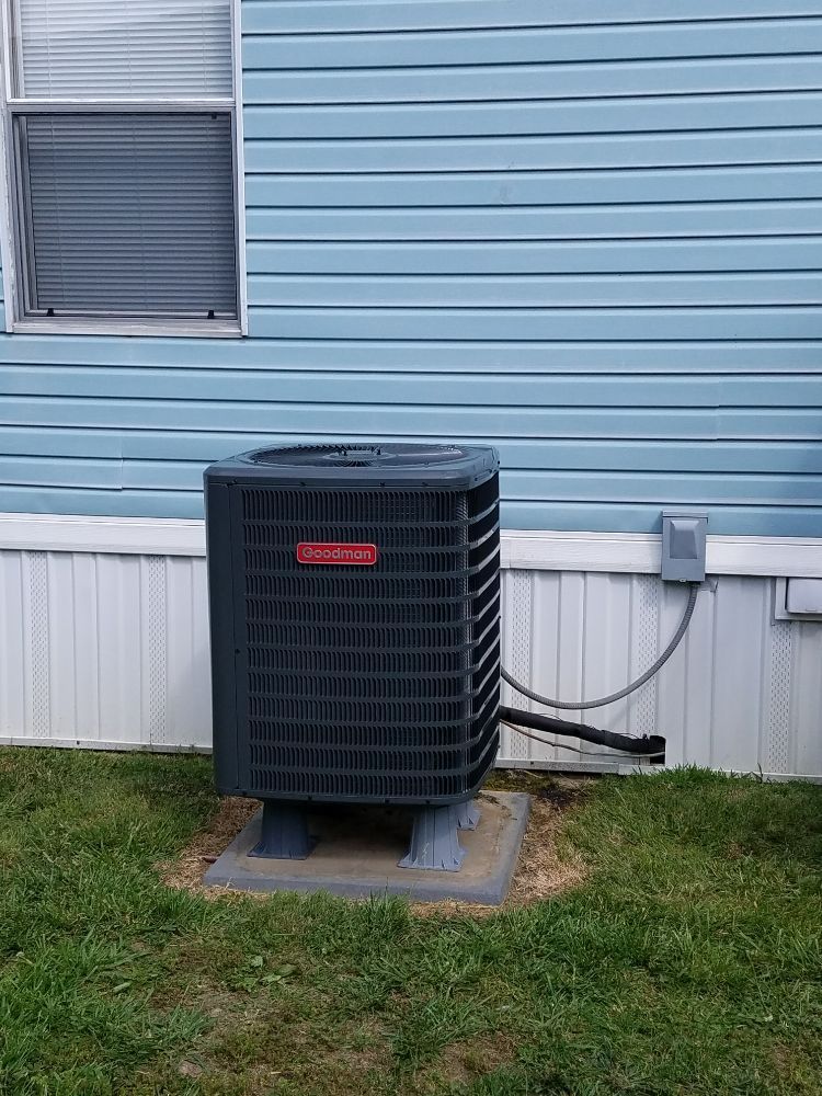 Black Goodman air conditioner unit outside a blue building, in a grassy yard.