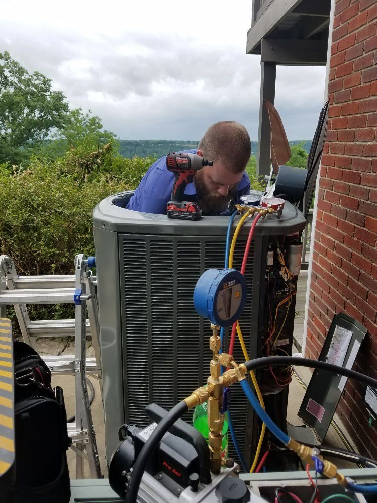 HVAC technician working on an AC unit outdoors with tools; gauges and a drill.