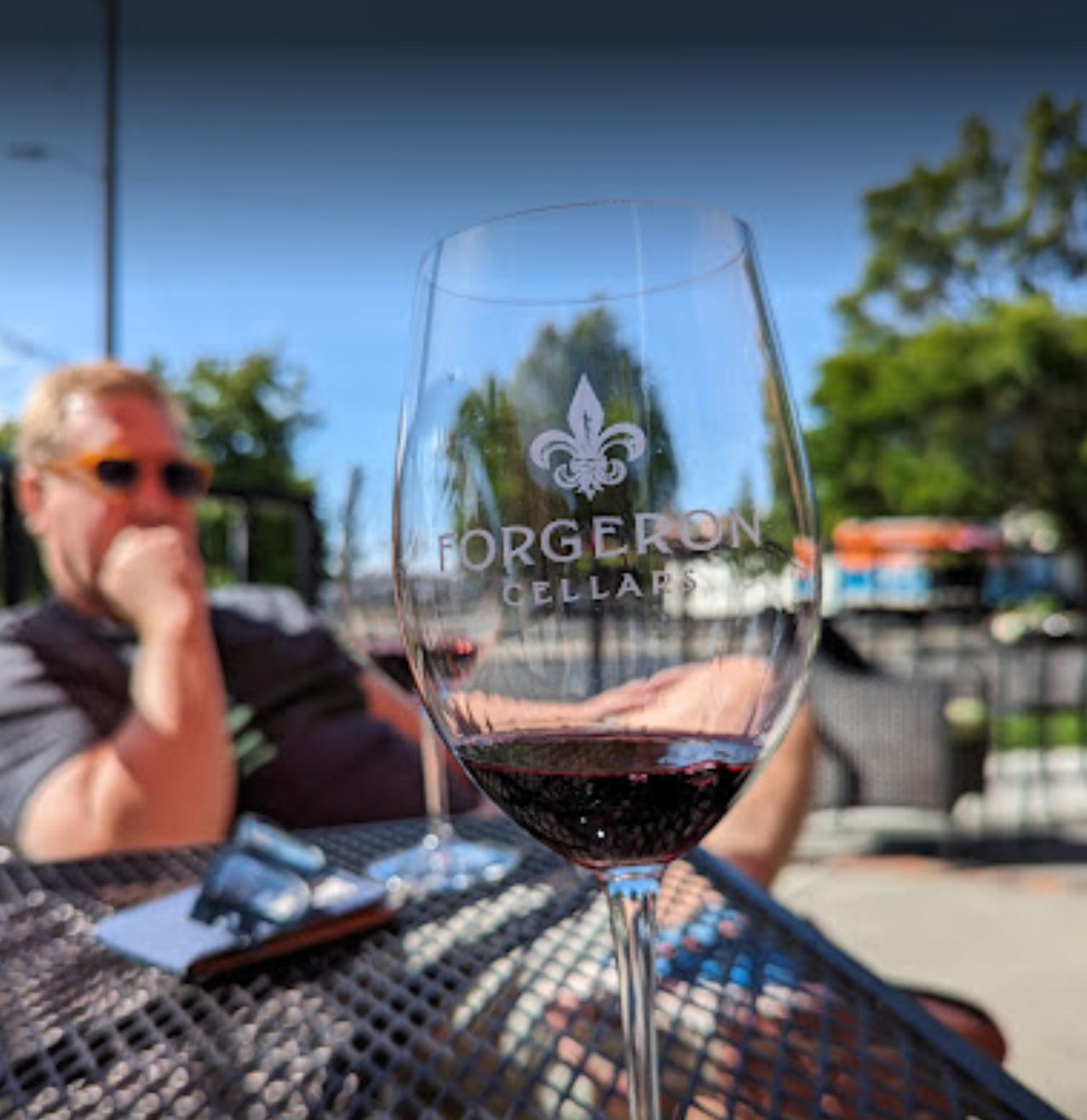 A man sits at a table with a glass of wine that says georgeron